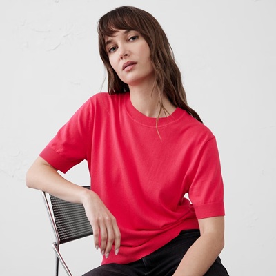 A woman sitting on a chair, wearing black pants and a coral short-sleeved sweater