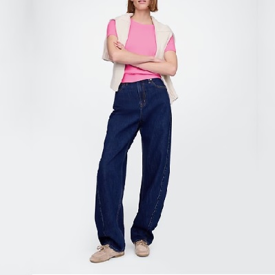 A woman wearing a light pink top and dark blue denim pants with cream sneakers