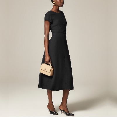 A woman wearing a black dress and black pointed heels with white hand bag