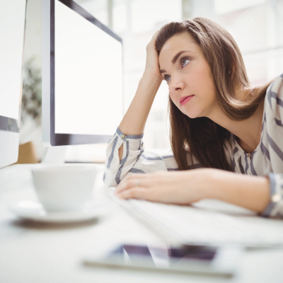 professional young woman looks exhaustedly at her computer screens while she tries to power through the afternoon slump in the workday