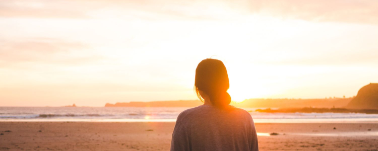 woman stands on beach looking at sun; she's wishing she had bought a sunscreen kit set to try in 2025