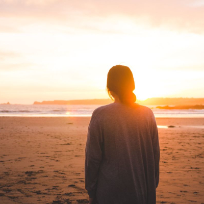 woman stands on beach looking at sun; she's wishing she had bought a sunscreen value set to try