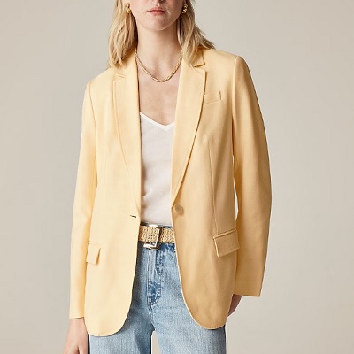 A woman wearing a white inner top with yellow blazer top and light denim pants