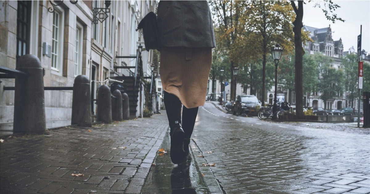 woman walks on city streets; photo shows her from the waist down, walking away from the camera