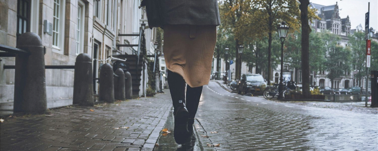woman walks on city streets; photo shows her from the waist down, walking away from the camera