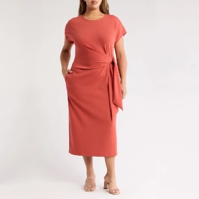A woman wearing a peach tie waist midi dress with cream block heels