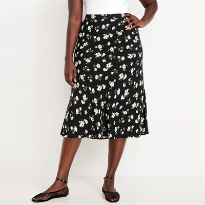 A woman wearing a white top, black-and-white floral midi skirt, and black mesh flats