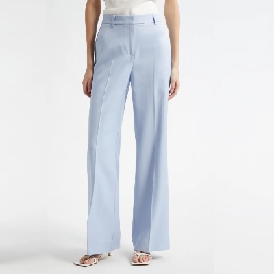 A woman wearing a white top and baby blue wide leg pants with white sandals