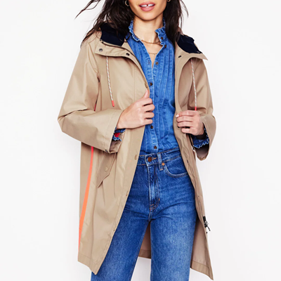 woman wears dark beige trenchcoat with orange stripe along side