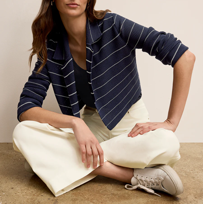 woman sits cross-legged on ground, she wears a striped sweater jacket, navy tank top, off-white jeans, and very light gray sneakers