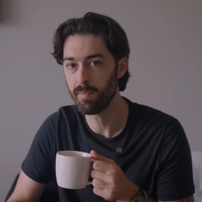 A man in a black tee looking at the camera and holding up a white coffee mug