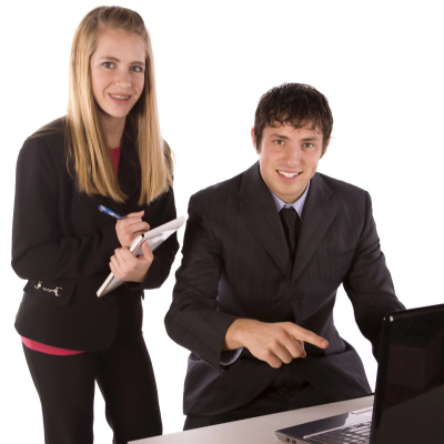 very young summer interns look eager and wear suits; she has long blond hair and is holding a notebook and pen, while he is wearing a suit and pointing at the computer screen