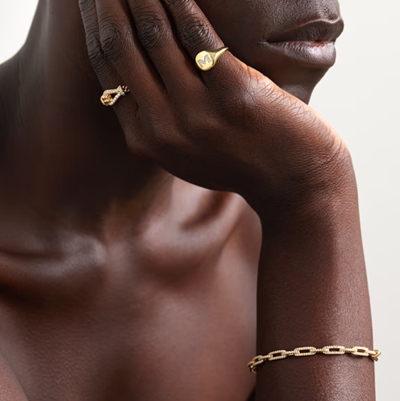 Black model wears gold initial pinky ring as well as another gold ring and gold bracelet