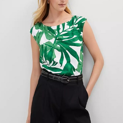 A woman wearing a white green floral printed top and black pants with black belt