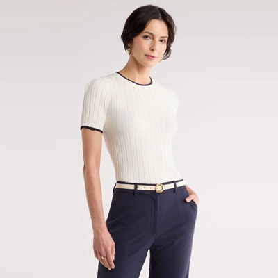 A woman wearing navy pants, a cream colored belt, and an ivory short-sleeved sweater with navy tipping