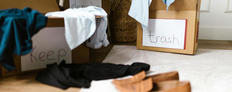 someone is updating their closet; there are 3 boxes on the floor with clothes spilling out of them and they are labeled KEEP, DONATE, and TRASH