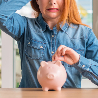 stressed out woman puts money into a piggy bank; she might be suffering from money dysmorphia where she feels poorer than she is (or richer than she is)