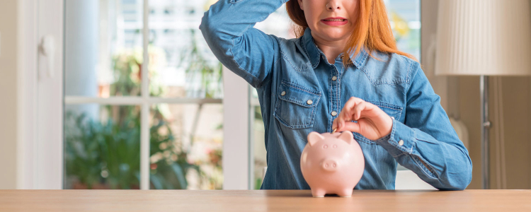 stressed out woman puts money into a piggy bank; she might be suffering from money dysmorphia where she feels poorer than she is (or richer than she is)
