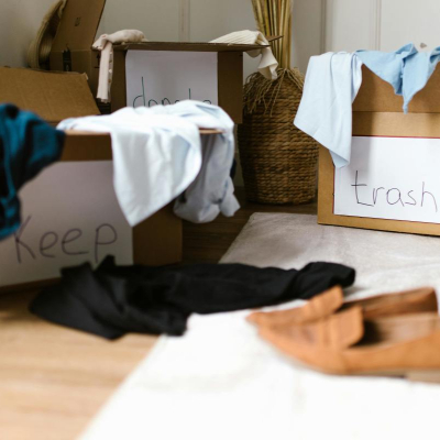 someone is updating their closet; there are 3 boxes on the floor with clothes spilling out of them and they are labeled KEEP, DONATE, and TRASH