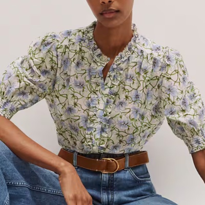 A woman wearing a floral printed blouse and denim pants with brown belt