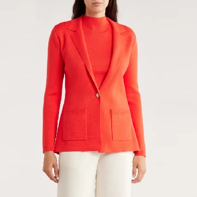 A woman wearing an orange top with orange blazer and white pants