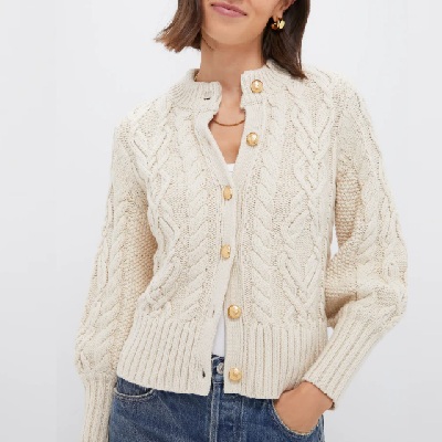 A woman wearing an ivory cable cardigan sweater and denim pants