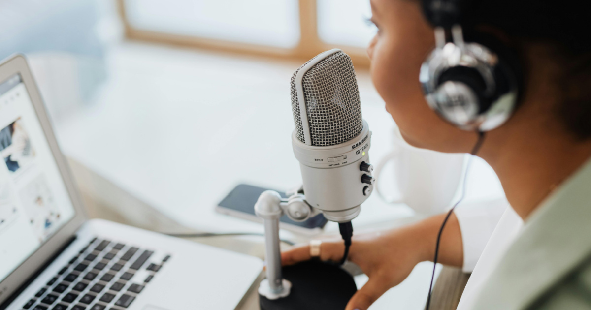 A woman at a computer wearing headphones and speaking into a mic