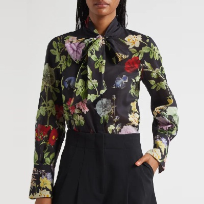A woman wearing a floral print long sleeve tie-neck top and black pants