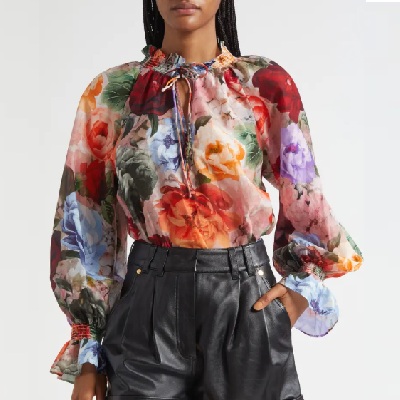 A woman wearing a floral printed silk top with black leather shorts