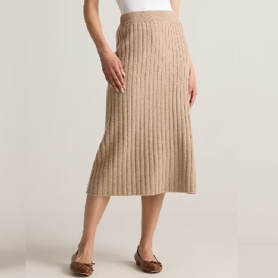 A woman wearing a beige midi skirt with brown flats