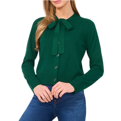 A woman wearing a green tie-neck cardigan and blue jeans