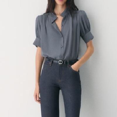 A woman wearing a gray chiffon top and denim trousers