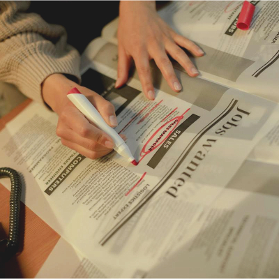 A woman sitting a desk in front of the newspaper classifieds. She has a red marker and has circled a job ad