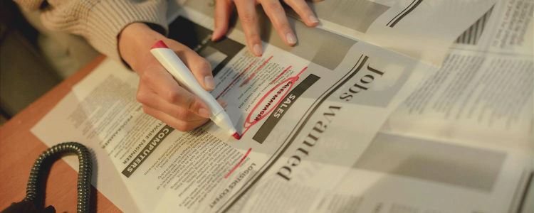 A woman sitting a desk in front of the newspaper classifieds. She has a red marker and has circled a job ad