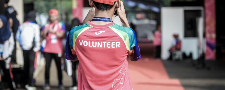 person wearing a red shirt that reads VOLUNTEER is taking a picture of a group of people; they might have found a great low commitment volunteer opportunity