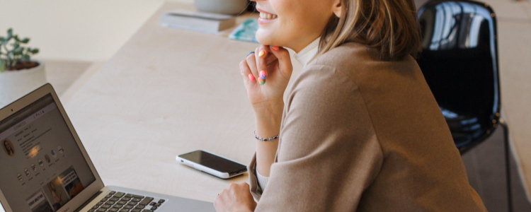 woman smiles wistfully at a laptop; the businesswoman has left corporate life and is happily working on her own time