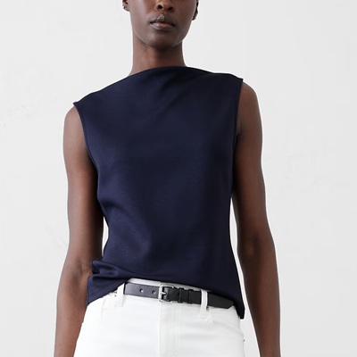 A woman wearing a navy sleeveless silk top with white pants and black belt
