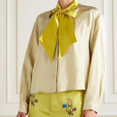 A woman wearing a light yellow satin long-sleeve blouse with yellow bow, with yellow floral-print pants