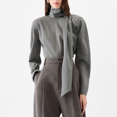 A woman wearing a gray long sleeve reversed scarf top with gray trouser pants