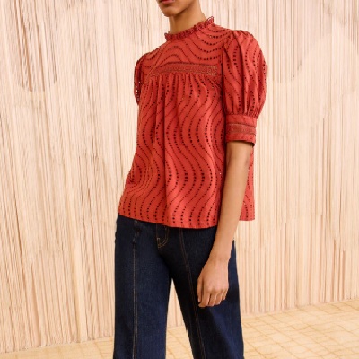A woman wearing a red puff short sleeve lace collar blouse and dark blue denim pants
