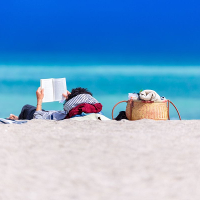 woman relaxes on beach with a book; she just might be a lawyer on a paid sabbatical from her job
