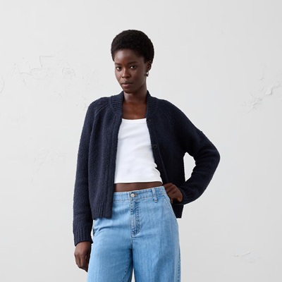 A woman wearing a white top, light blue jeans, and a navy cardigan