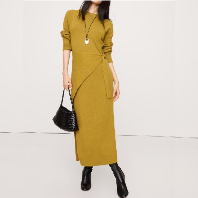 A woman wearing a mustard long sleeve dress with black high boots and black bag