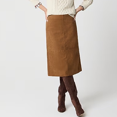 A woman wearing a brown suede midi skirt with white knitted jacket and brown boots