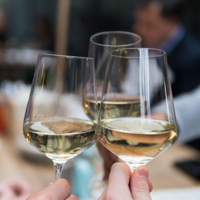 three people toast white wine in unmatched glasses; they just might be at a reunion