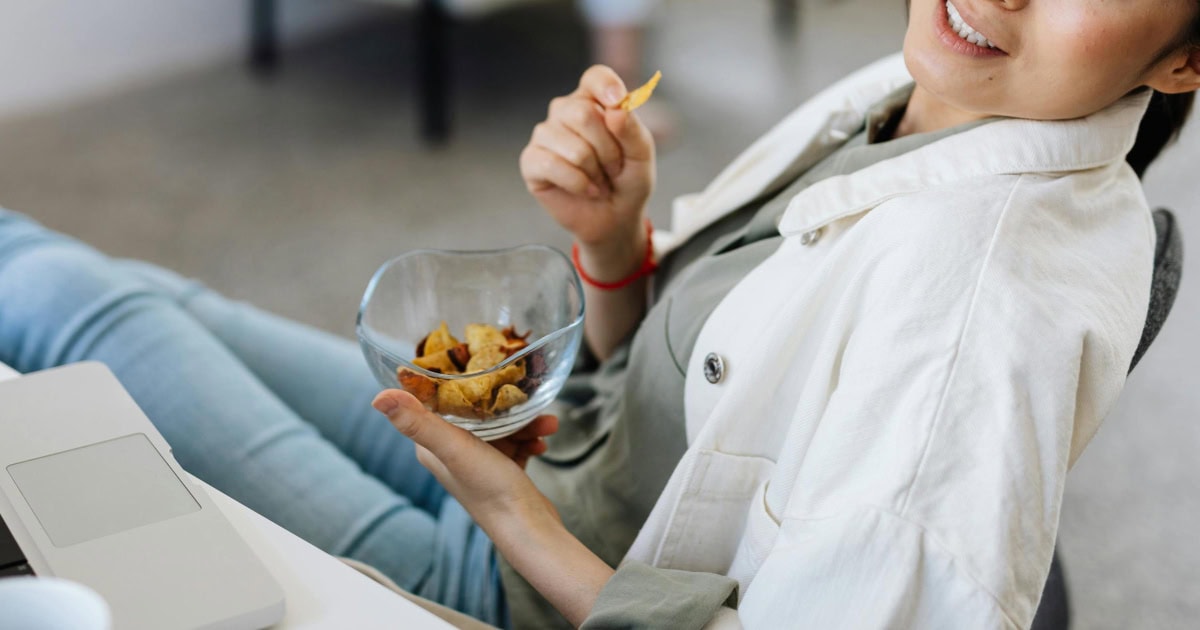 woman wearing business casual reclines in desk chair with some of the best office snacks