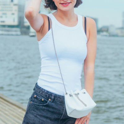 woman wears white tank top with her black bra straps showing; she is posing in front of a city pier