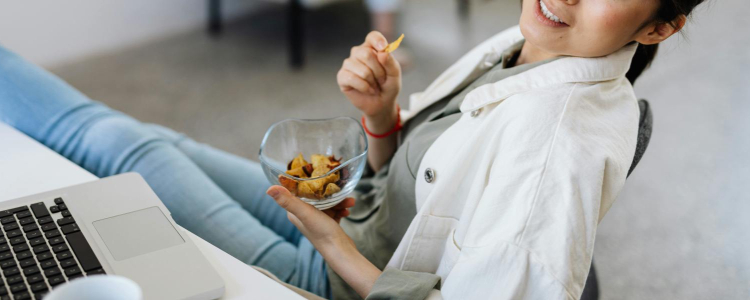 woman wearing business casual reclines in desk chair with some of the best office snacks