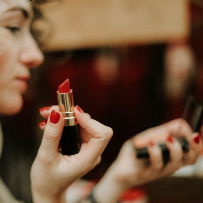 professional woman applies red lipstick using hand mirror