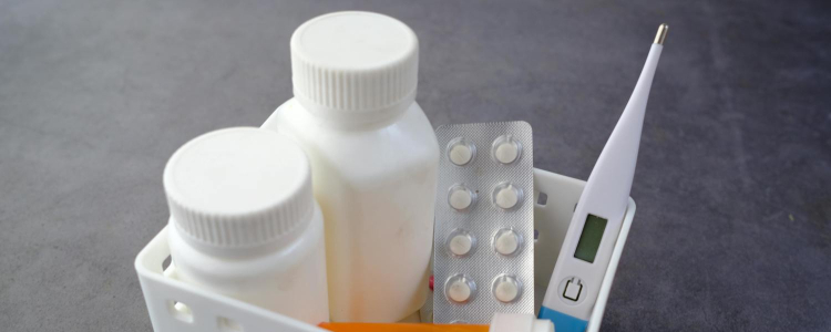 small container filled with pill bottles and packs and a thermometer